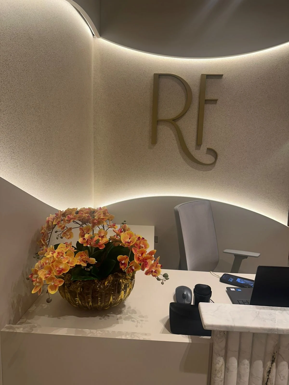 Recepção do Espaço Roberta Ferreira, com flores, iluminação suave e o monograma RF na parede